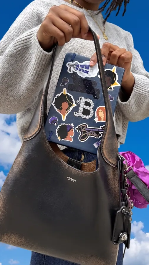 Leather bag carrying a notebook covered in Braid stickers